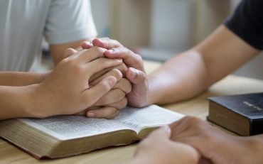 Prayer meeting concept.Colleagues shaking hands reading scriptures and praying to God at work place.